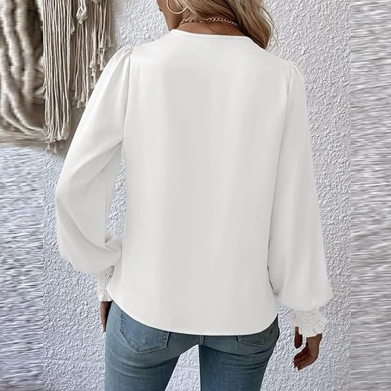 Donna con camicetta bianca a maniche lunghe, dettagli in pizzo, abbinata a jeans. Sfondo con parete bianca e decorazione tessile.