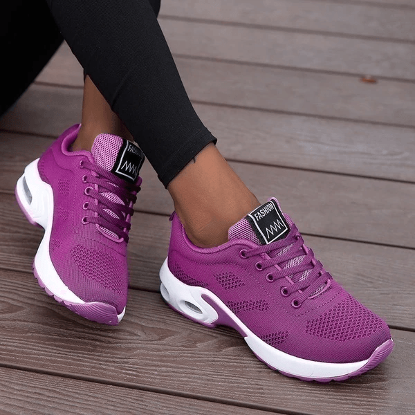 Scarpe da ginnastica viola da donna su pavimento in legno, design moderno e traspirante, ideali per sport e tempo libero.
