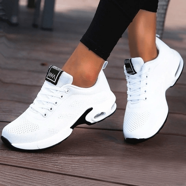 Scarpe da ginnastica bianche da donna su pavimento in legno, design moderno e traspirante, ideali per sport e tempo libero, comfort e stile.