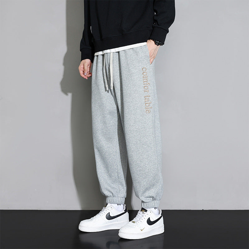 Pantaloni jogger grigi da uomo, comodi e casual, con scritta "comfortable" sulla gamba. Abbinati a sneakers bianche Nike e felpa nera.