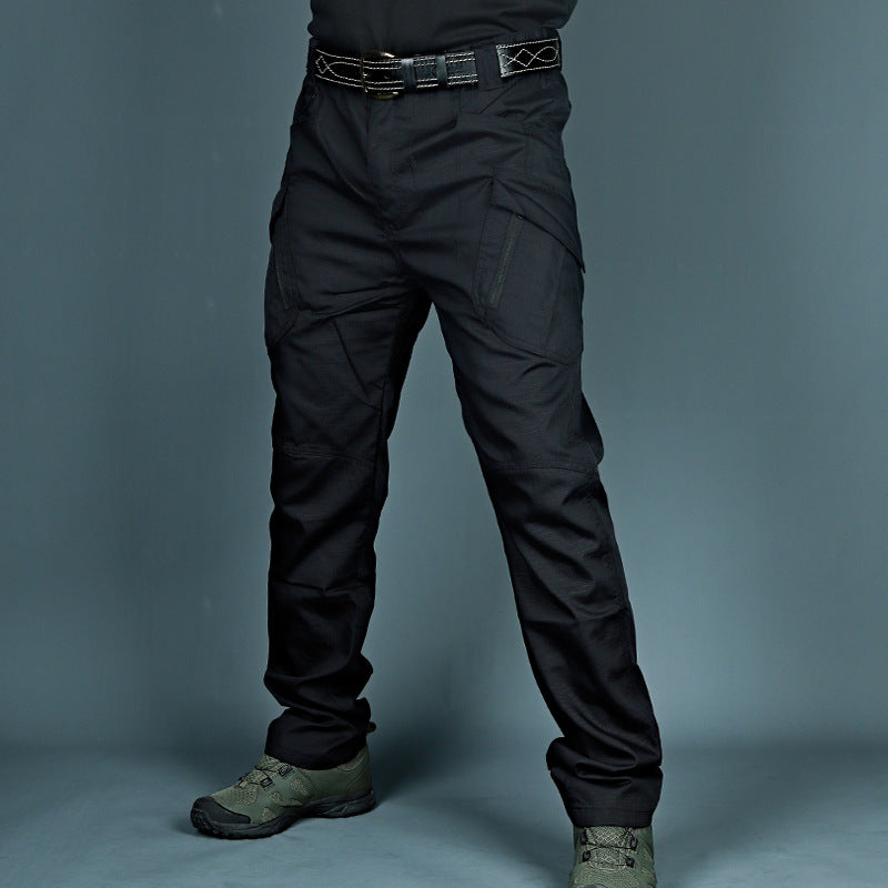Pantaloni tattici neri con tasche multiple, indossati con cintura robusta e scarpe militari verdi. Abbigliamento outdoor resistente e funzionale.