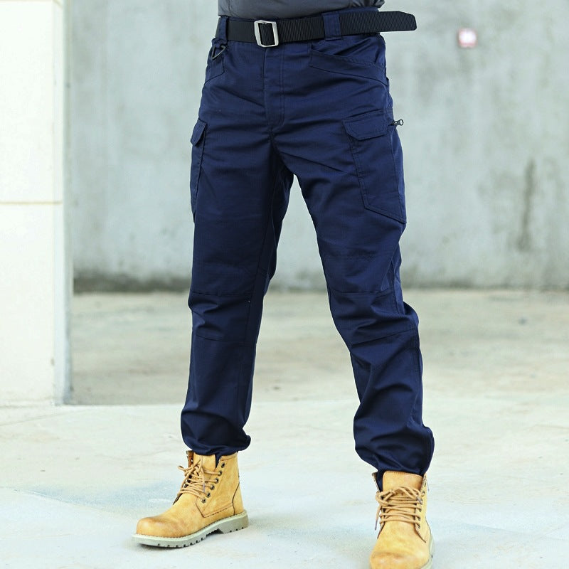 Pantaloni tattici blu scuro con tasche multiple, indossati con stivali gialli robusti. Abbigliamento outdoor resistente e funzionale.