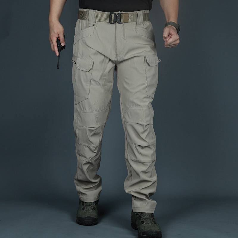 Pantaloni tattici beige con tasche multiple, indossati da una persona in piedi su sfondo grigio. Ideali per attività outdoor e avventure.