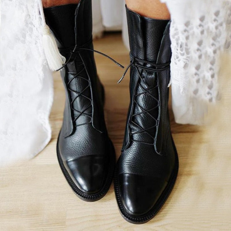 Stivali neri in pelle con lacci su pavimento in legno, indossati con abito bianco in pizzo. Scarpe eleganti e moderne per look autunnale.