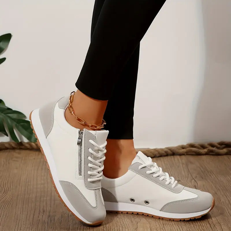 Scarpe da ginnastica bianche e grigie con cerniera laterale, indossate con leggings neri su pavimento in legno. Sneakers moda donna, stile casual.