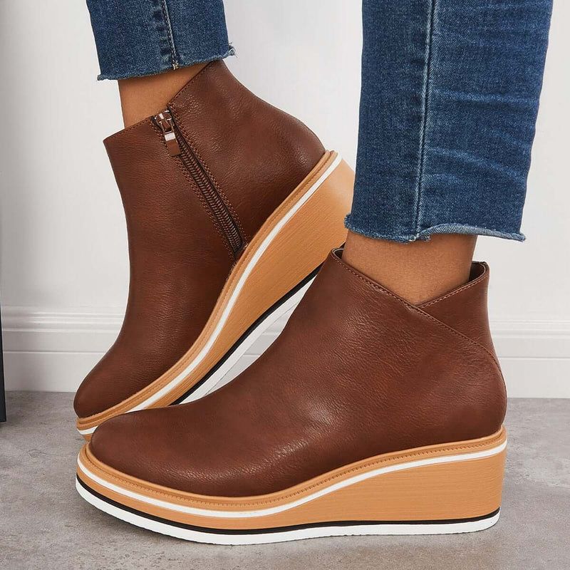 Stivaletti donna marroni con zeppa, chiusura a zip, suola in gomma bianca e dettagli in legno, abbinati a jeans blu. Moda calzature autunno inverno.