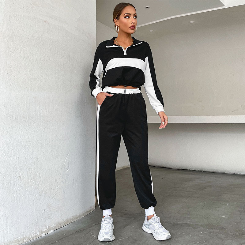 Donna in tuta sportiva nera e bianca, scarpe da ginnastica bianche, posa in un ambiente moderno. Abbigliamento casual, moda donna, stile athleisure.