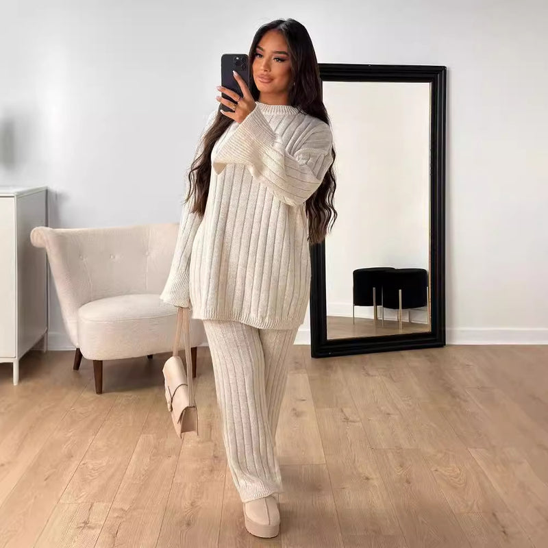 Donna con maglione e pantaloni a coste bianchi, scatta selfie davanti a specchio grande. Arredamento minimalista, pavimento in legno chiaro.