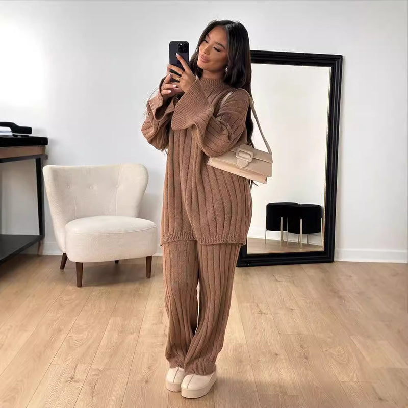 Donna in salotto moderno indossa completo maglia marrone, borsa beige, specchio grande, sedia bianca, pavimento in legno chiaro, scatta selfie.