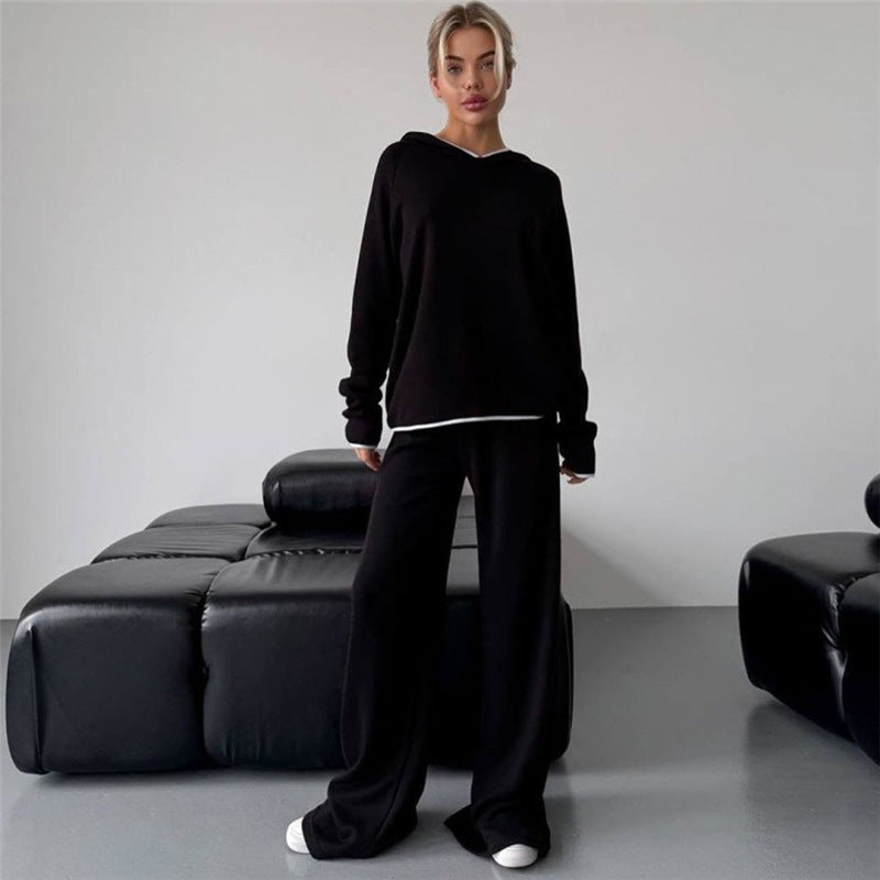 Donna in abbigliamento casual nero, felpa e pantaloni larghi, posa in un salotto moderno con divano in pelle nera. Stile minimalista, moda urbana.
