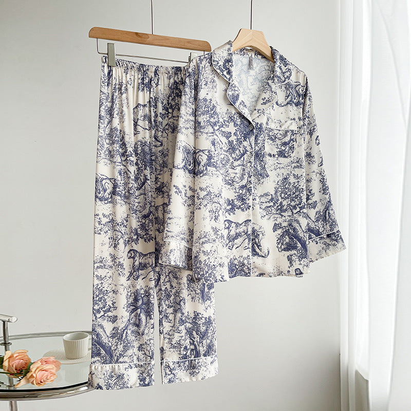 Pigiama donna in raso bianco con stampa blu a motivi floreali e animali, appeso su grucce. Elegante e confortevole, ideale per la notte.