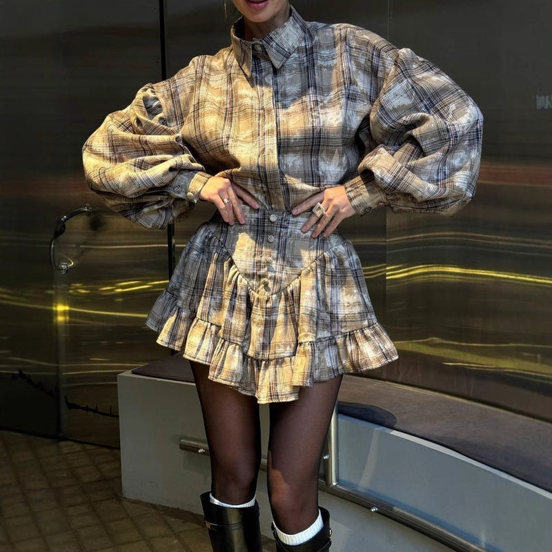 Donna con abito a quadri marrone e beige, maniche ampie, gonna a balze, stivali neri e calze bianche. Moda autunnale elegante e moderna.