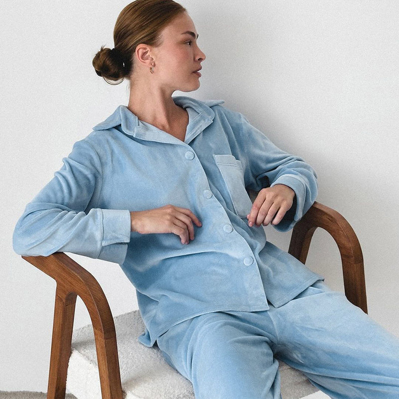 Donna seduta su sedia in pigiama azzurro di velluto, design elegante e confortevole, moda notte, abbigliamento da casa, stile rilassato e moderno.