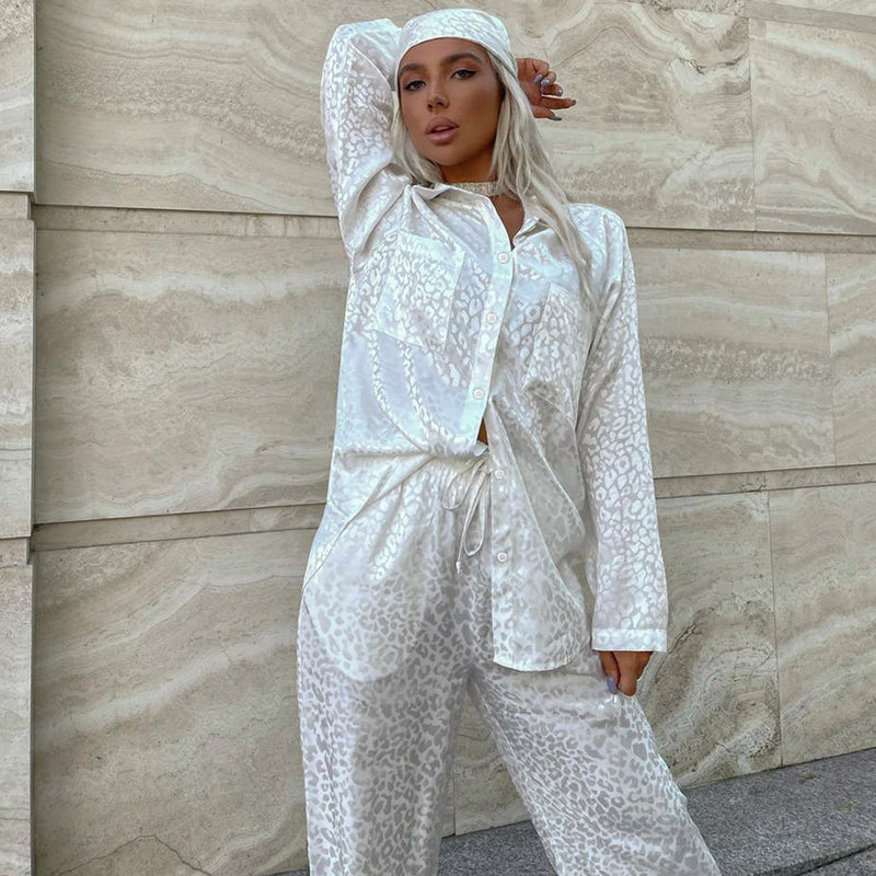 Donna in pigiama di seta bianco con stampa leopardata, posa elegante contro un muro di pietra. Moda femminile, abbigliamento notte di lusso.