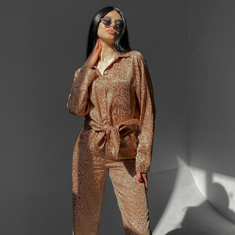 Donna con occhiali da sole indossa pigiama leopardato marrone in raso, posa con mano sui capelli. Moda femminile, abbigliamento notte elegante.