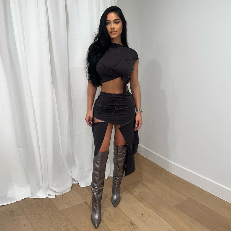 Donna con abito nero elegante e stivali alti grigi, posa su pavimento in legno chiaro, sfondo con tende bianche. Moda femminile, stile moderno.