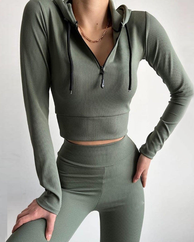 Donna in abbigliamento sportivo verde oliva, con felpa corta a zip e pantaloni aderenti. Moda fitness, abbigliamento activewear elegante.