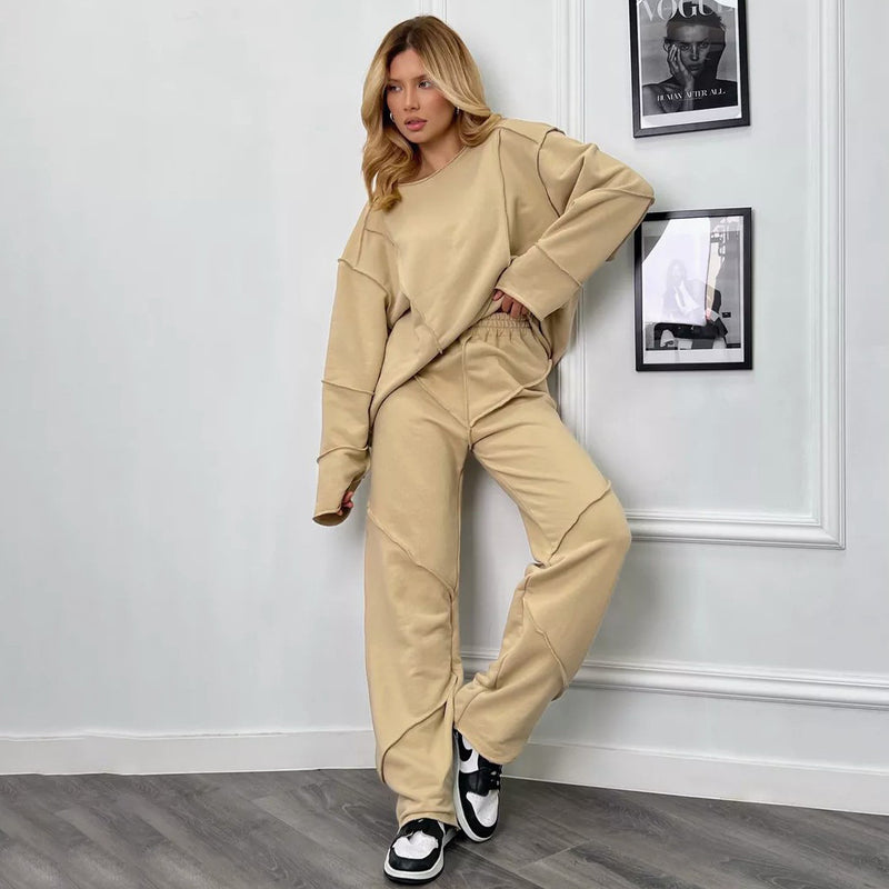 Donna in tuta beige alla moda, posa in interni moderni. Abbigliamento casual, scarpe da ginnastica bianche e nere. Stile contemporaneo.
