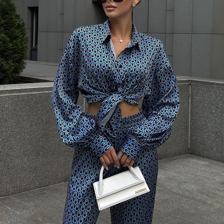 Donna con camicia e pantaloni blu a fantasia geometrica, borsa bianca Jacquemus, sfondo urbano grigio. Moda elegante, street style.