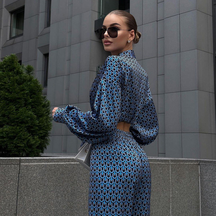 Donna elegante in abito blu a fantasia geometrica, occhiali da sole, posa davanti a edificio moderno. Moda urbana, stile sofisticato.