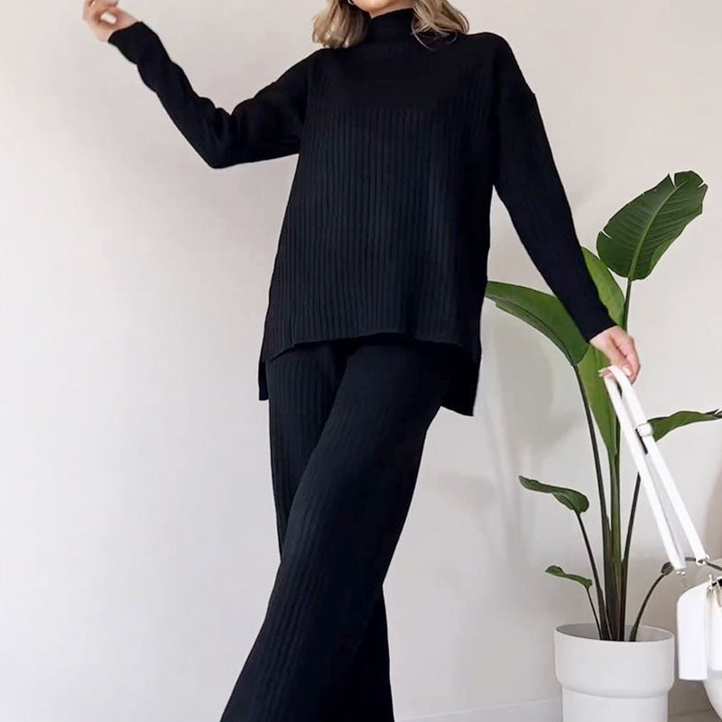 Donna in abbigliamento nero elegante, maglione e pantaloni a coste, accanto a pianta d'appartamento. Moda minimalista, outfit autunnale.
