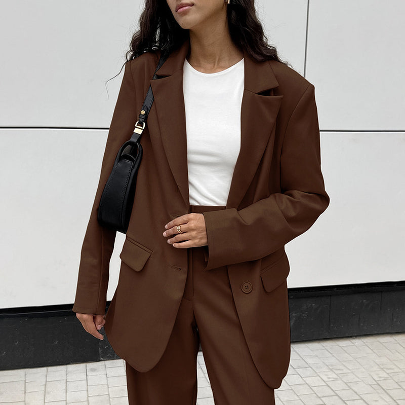 Donna con blazer marrone e borsa nera, indossa una maglietta bianca. Moda autunnale elegante, stile casual chic. Sfondo urbano minimalista.