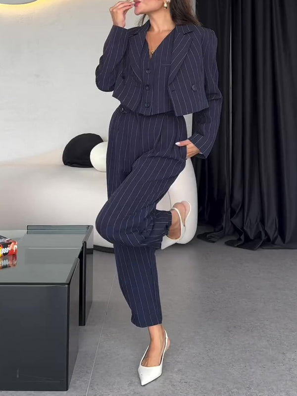 Donna in elegante completo gessato blu scuro, giacca e pantaloni, posa in salotto moderno. Moda femminile, abbigliamento formale, stile contemporaneo.