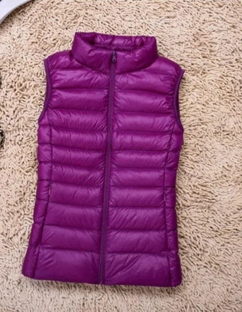 Gilet imbottito viola su tappeto beige, senza maniche, con zip frontale. Moda autunno inverno, abbigliamento casual, giacca leggera donna.