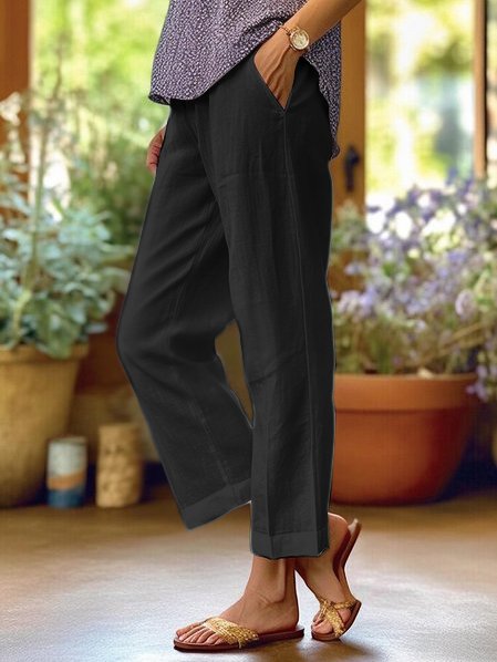 Donna in pantaloni neri larghi, sandali dorati, in piedi su una veranda con piante in vaso. Moda casual estiva, abbigliamento comodo.