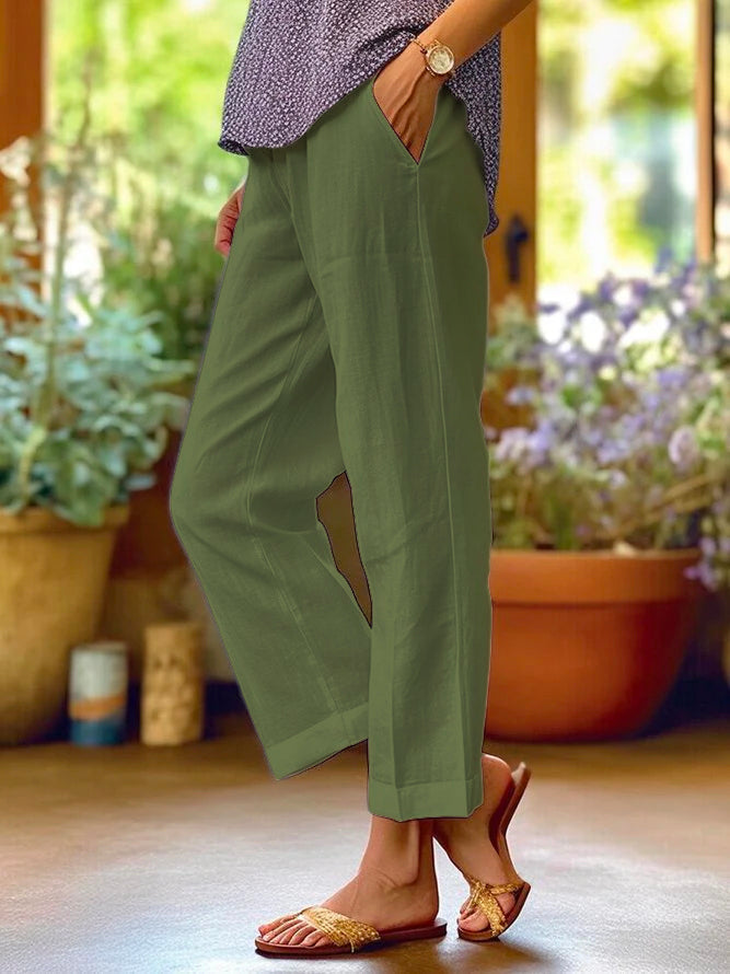 Pantaloni verdi da donna in lino, comodi e casual, abbinati a sandali estivi. Perfetti per look estivo rilassato. Sfondo con piante in vaso.