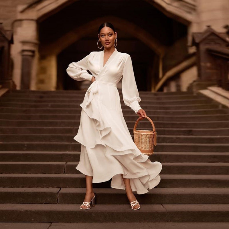 Donna elegante in abito bianco con volant su scala storica, borsa di paglia, orecchini a cerchio. Moda femminile, stile sofisticato, abbigliamento chic.