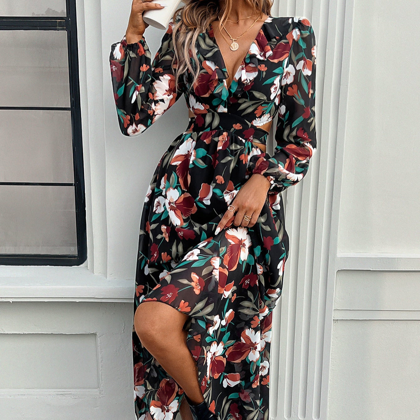 Abito lungo floreale nero con scollo a V e maniche lunghe, indossato da una donna davanti a una finestra. Moda autunnale elegante e femminile.