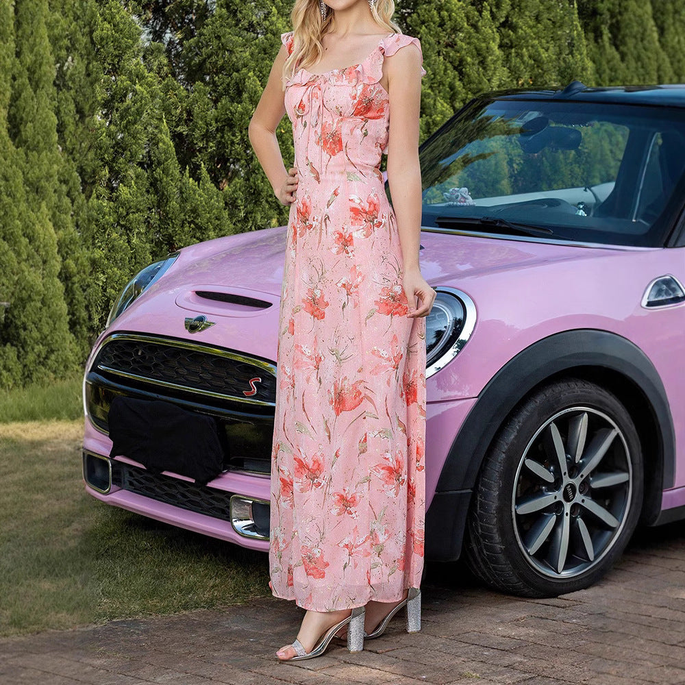 Donna in abito floreale rosa accanto a Mini Cooper rosa, su strada con alberi sullo sfondo. Auto elegante, moda estiva, stile casual chic.