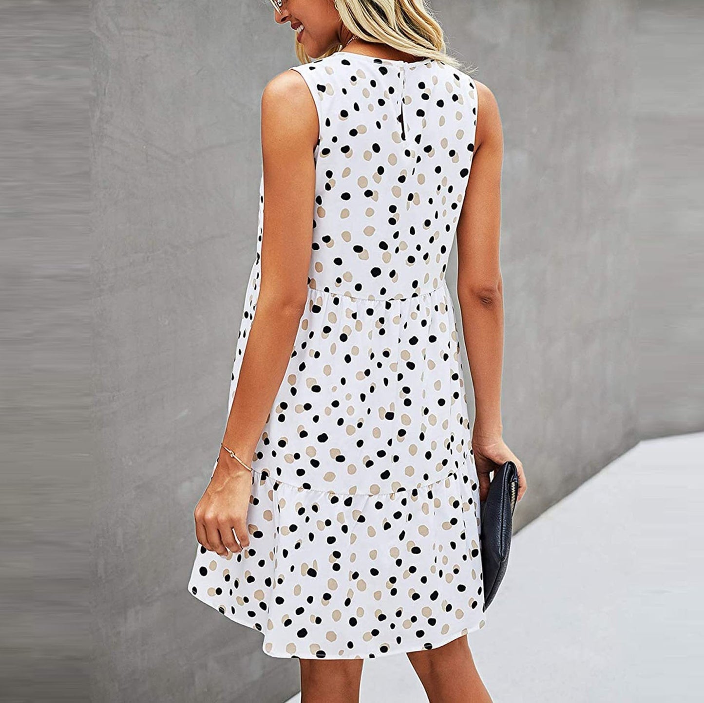 Abito estivo a pois bianchi e neri, senza maniche, indossato da una donna bionda. Moda casual elegante, perfetto per giornate calde.