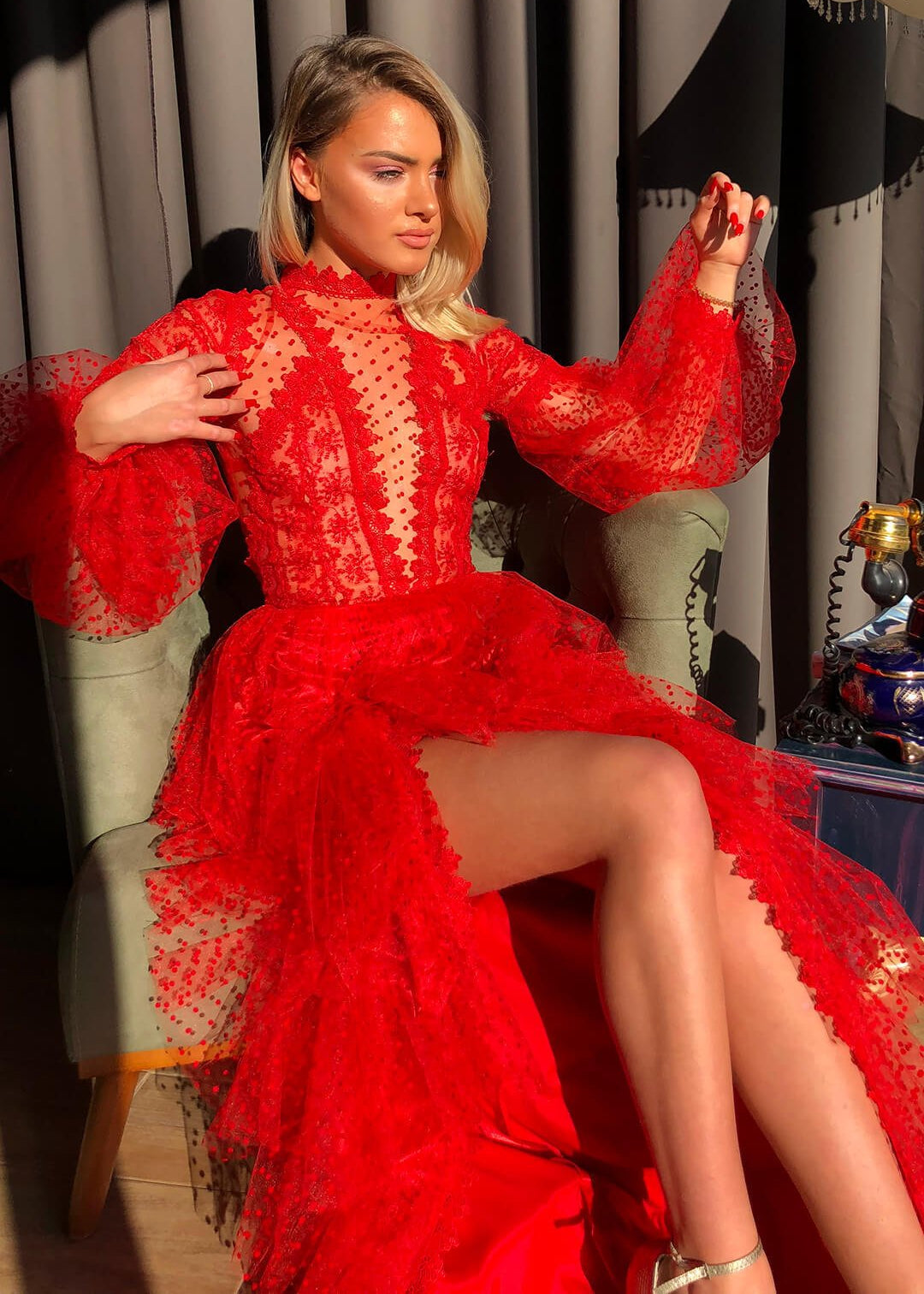 Donna in abito rosso elegante con dettagli in pizzo, seduta su poltrona. Moda femminile, abbigliamento da sera, stile glamour.