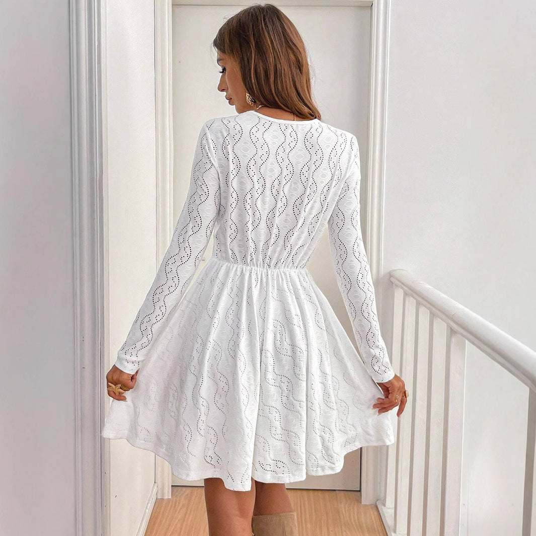Donna in abito bianco elegante, maniche lunghe, motivo traforato, in piedi su una scala interna. Moda femminile, abbigliamento chic, stile moderno.