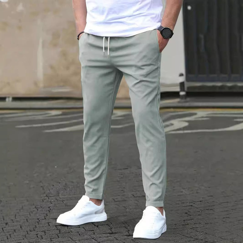 Uomo in pantaloni sportivi grigi e scarpe da ginnastica bianche su strada asfaltata. Look casual, moda maschile, abbigliamento urbano.