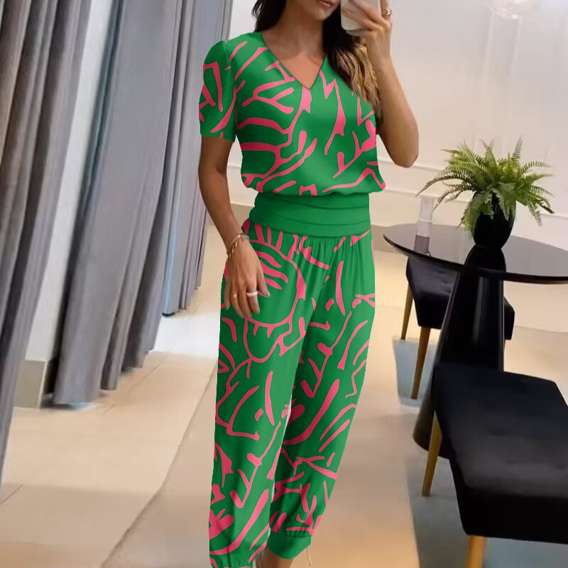 Donna in salotto indossa tuta verde con motivi rosa, scatta selfie. Moda casual, abbigliamento estivo, design moderno. Arredamento elegante.