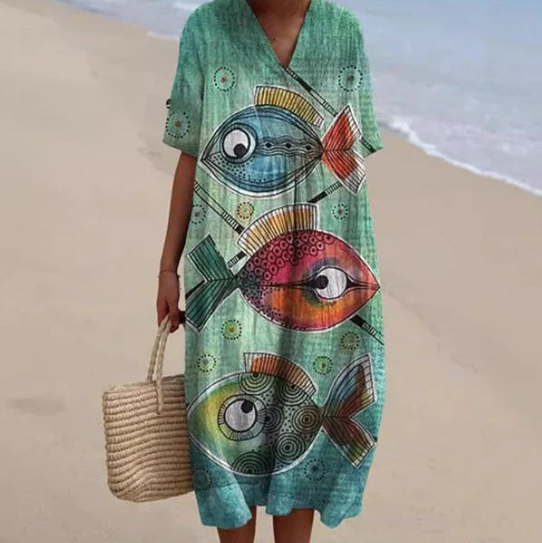 Abito estivo con stampa di pesci colorati su sfondo verde, indossato su una spiaggia. Moda mare, abbigliamento casual, stile vacanza.