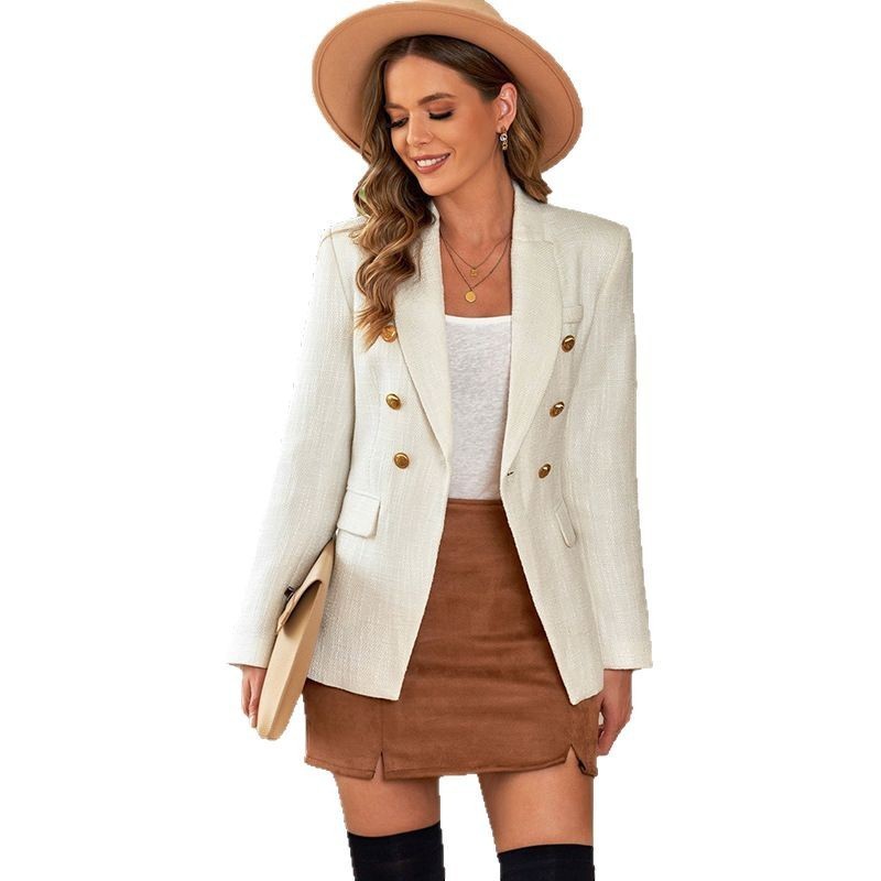 Donna con cappello beige, blazer bianco a doppiopetto, top bianco, gonna marrone e stivali neri. Moda autunnale elegante e casual.