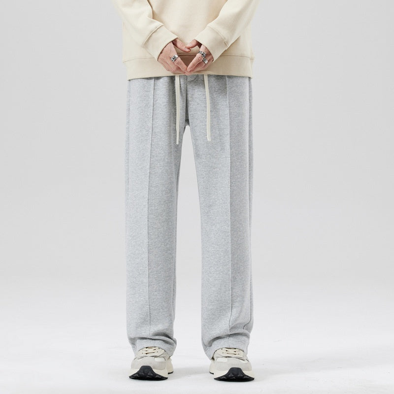 Pantaloni tuta grigi uomo, stile casual, con coulisse, abbinati a felpa beige e sneakers bianche. Moda streetwear, abbigliamento comodo.