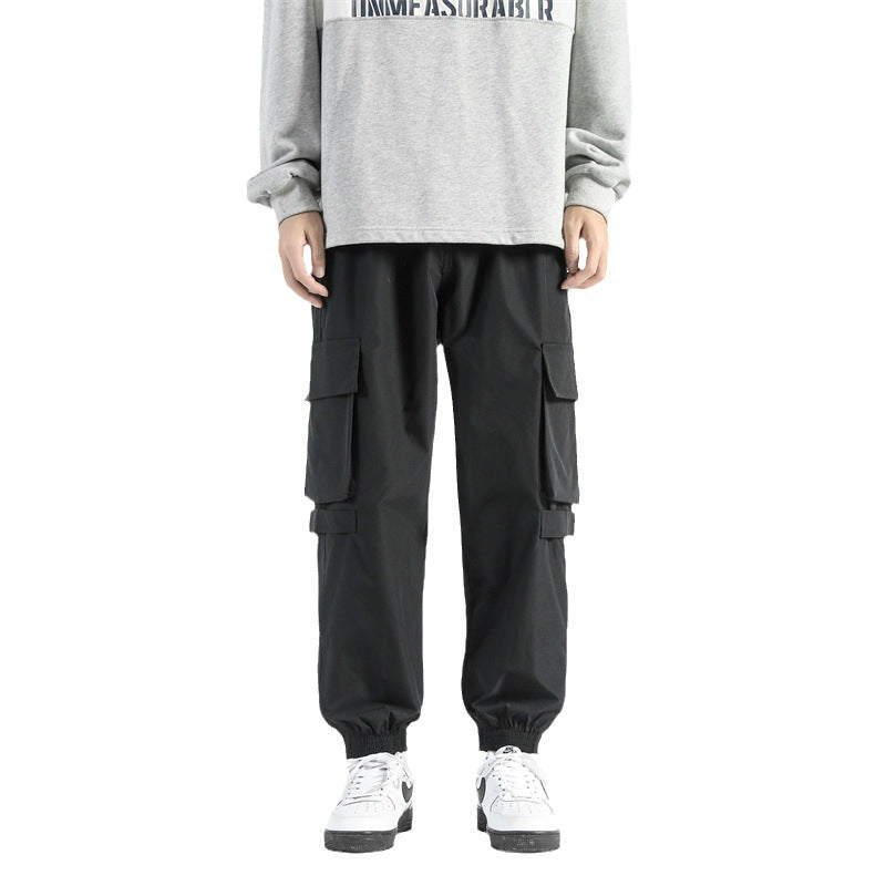 Pantaloni cargo neri da uomo con tasche multiple, abbinati a felpa grigia e scarpe da ginnastica bianche. Stile casual e moderno.