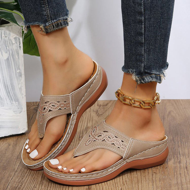 Sandali beige da donna con zeppa, dettagli traforati, indossati con jeans e cavigliera dorata. Scarpe estive eleganti e comode.