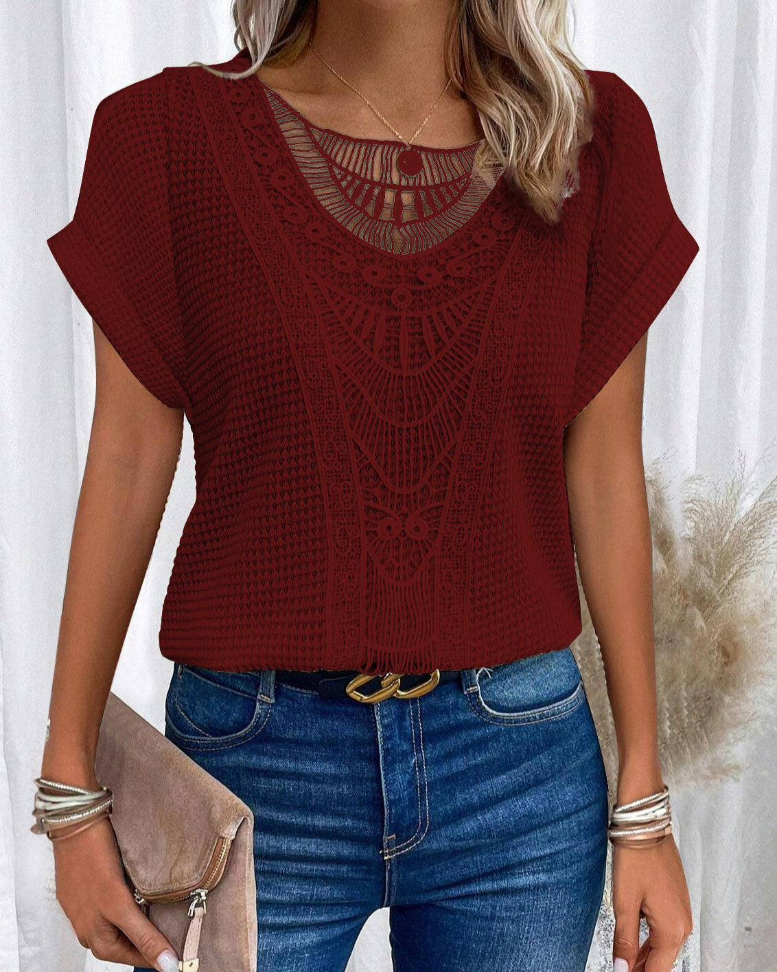 Donna con maglia rossa in pizzo, jeans blu, cintura nera e borsa beige. Stile casual elegante, moda femminile, abbigliamento estivo.