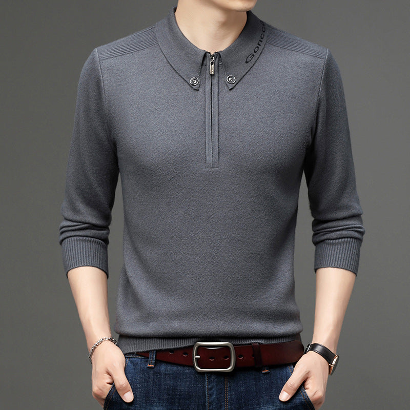 Maglione grigio da uomo con colletto alto e zip, abbinato a jeans blu e cintura marrone. Moda maschile elegante e casual.