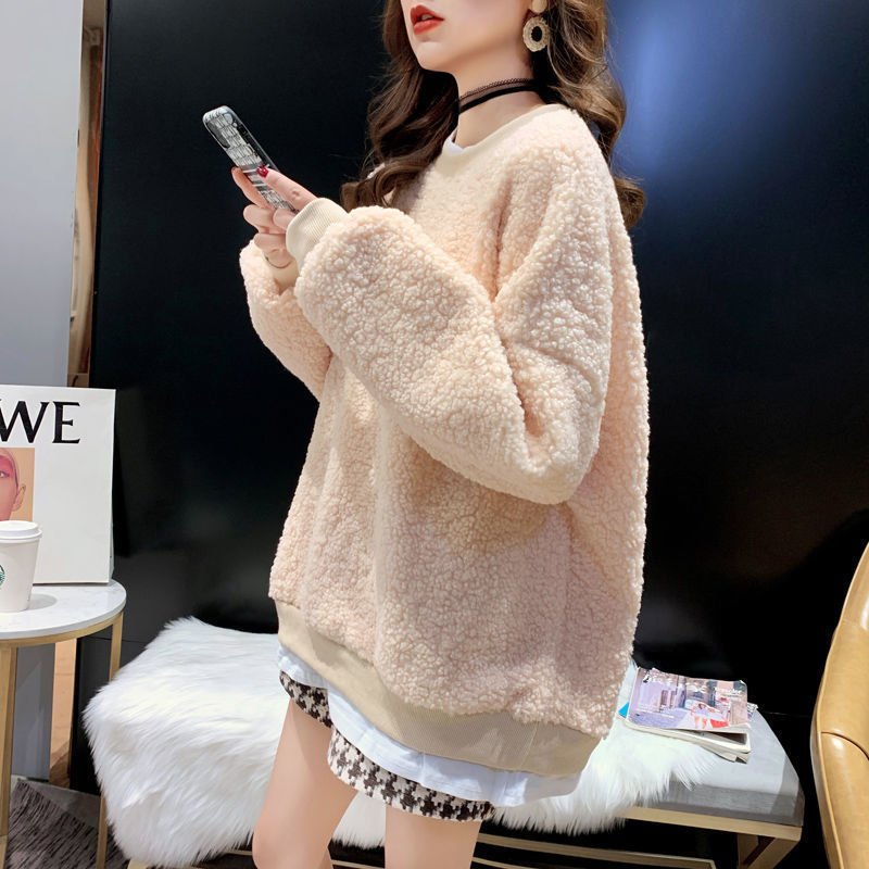 Donna con maglione in pile beige, smartphone in mano, seduta su sedia moderna. Moda invernale, abbigliamento casual, stile urbano.