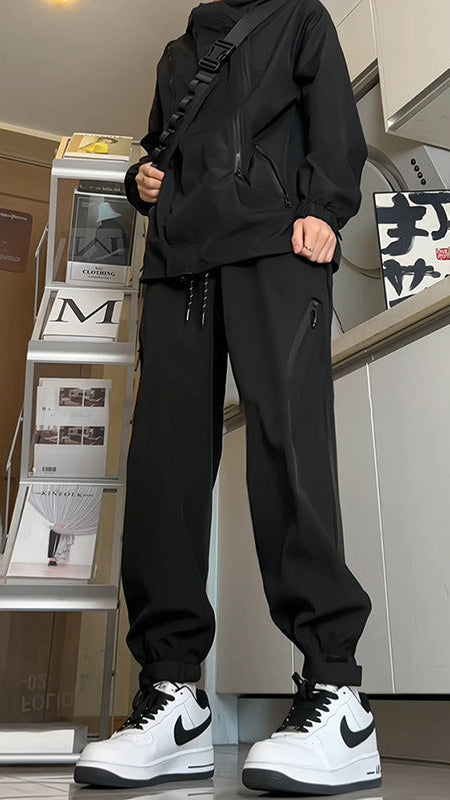 Uomo in abbigliamento sportivo nero con scarpe Nike bianche e nere, posa in una stanza moderna con scaffali e riviste. Moda streetwear casual.