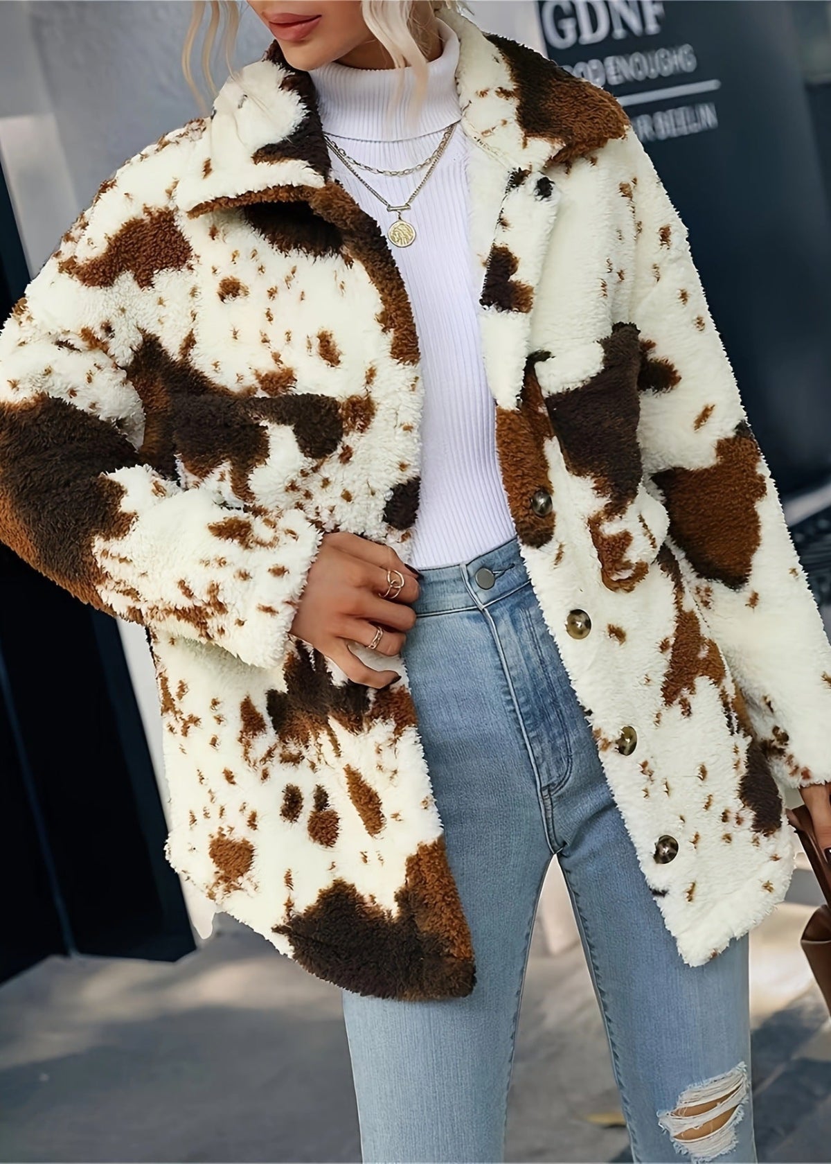 Giacca in pelliccia sintetica maculata bianca e marrone, indossata con jeans strappati e maglione bianco a collo alto. Moda autunnale casual.