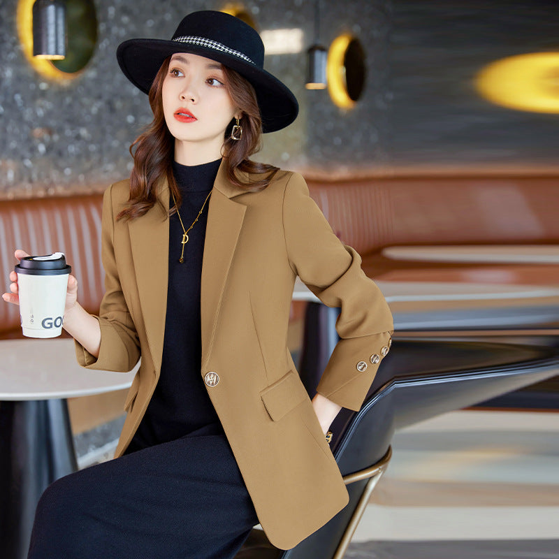 Donna elegante con cappello nero e blazer marrone, seduta in un caffè moderno, tiene una tazza da asporto. Moda autunnale, stile urbano chic.