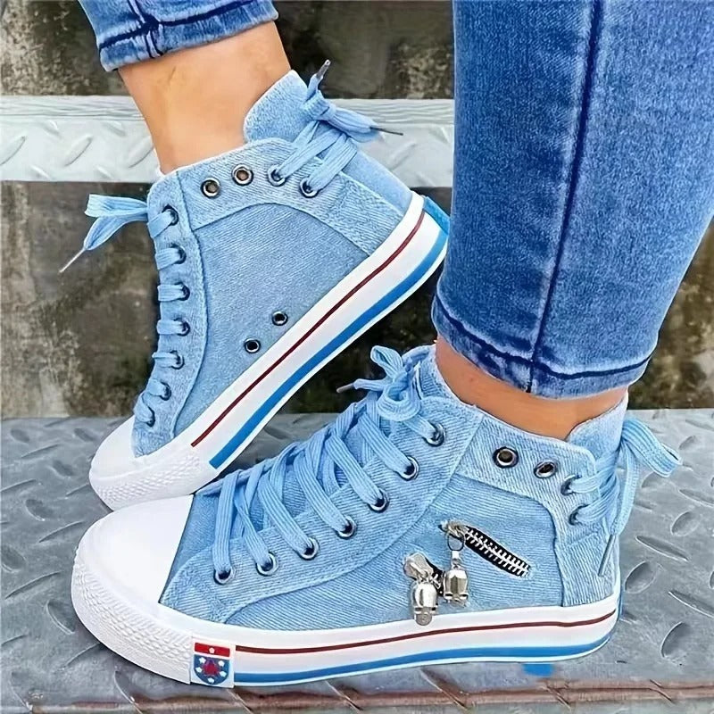 Scarpe da ginnastica alte in denim azzurro con lacci, zip decorativa e charm, indossate con jeans. Scarpe casual moda, stile urbano.
